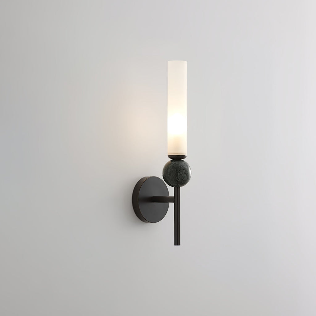 Lit and shown against grey, this Clérachic black-arm wall sconce carries a green marble orb on its arm.