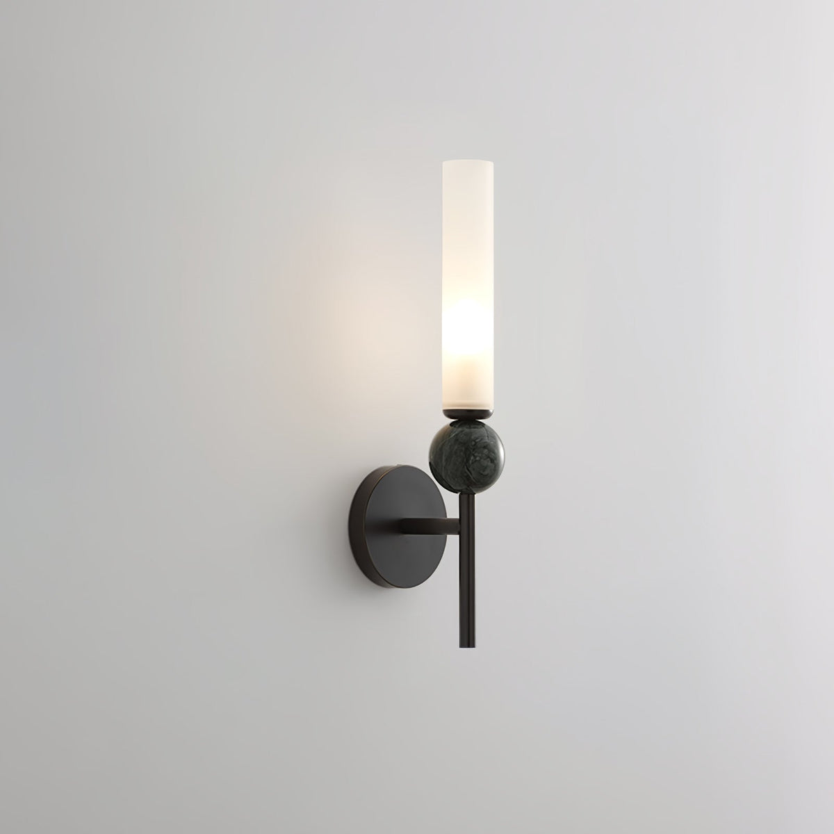Lit and shown against grey, this Clérachic black-arm wall sconce carries a green marble orb on its arm.