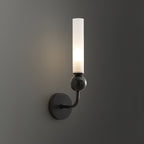A Clérachic black wall sconce with a black marble orb glows against a dark charcoal wall in a moodily lit room.