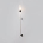 A tall Clérachic black vertical wall light glows at the top, standing full length against a plain grey background.