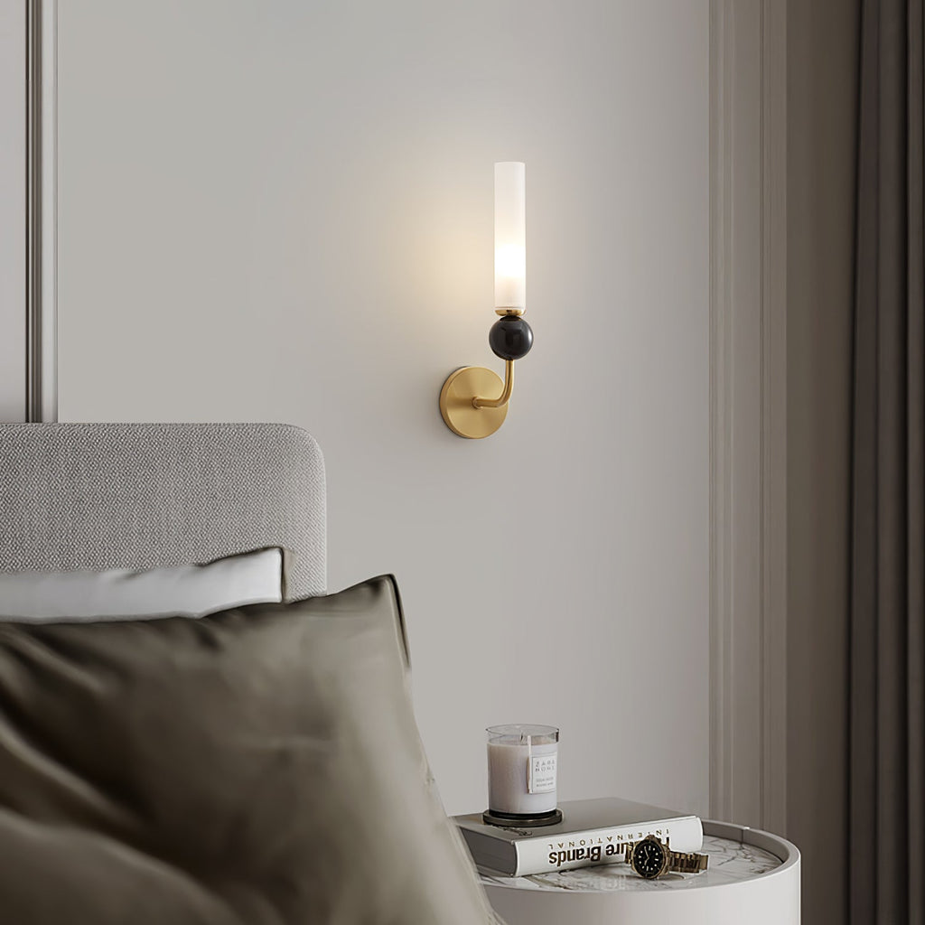 Close crop of a bed with an olive pillow and a candle on a round table, a Clérachic brass wall sconce glowing above the headboard.