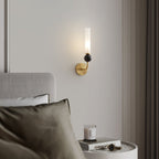 Close crop of a bed with an olive pillow and a candle on a round table, a Clérachic brass wall sconce glowing above the headboard.