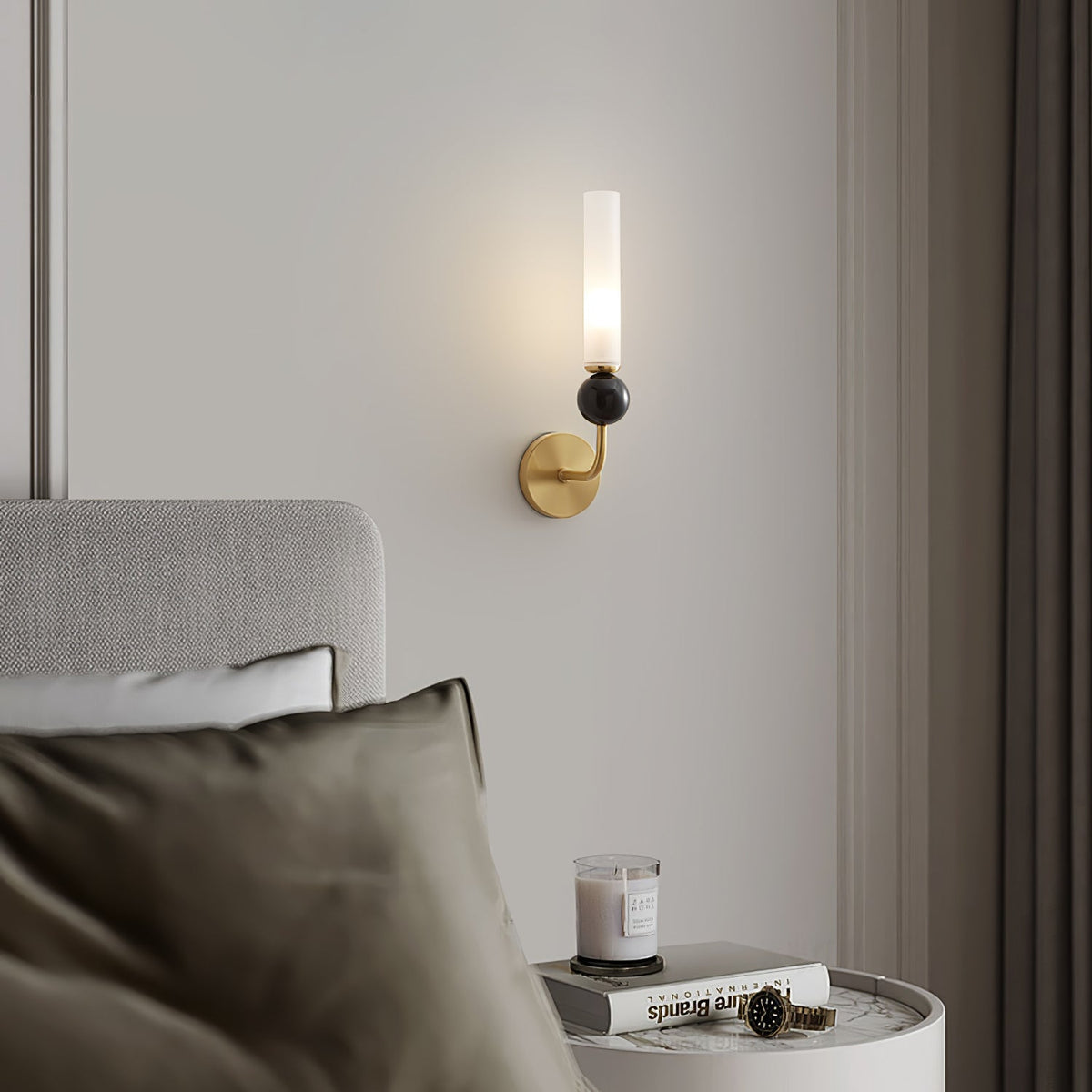 Close crop of a bed with an olive pillow and a candle on a round table, a Clérachic brass wall sconce glowing above the headboard.