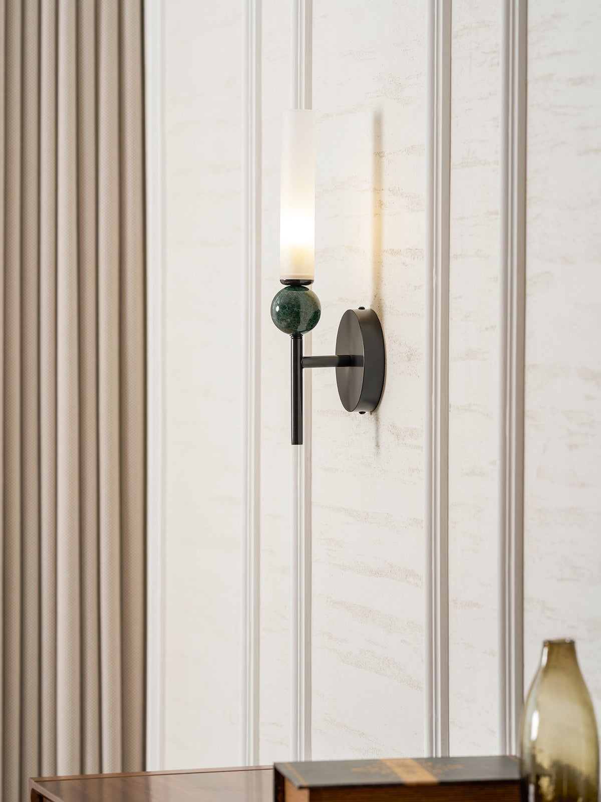 Lit above a walnut sideboard on a panelled wall, the Clérachic wall light throws a soft column of light up the moulding.