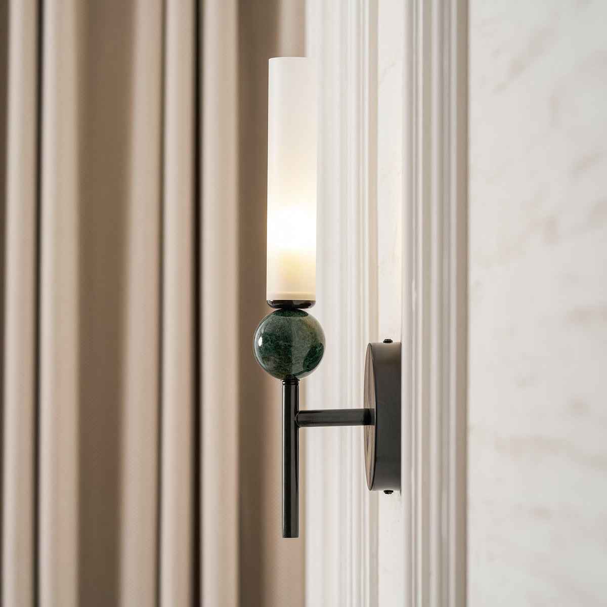 Close crop of the Clérachic wall light beside a linen curtain, the green marble sphere and black backplate filling the frame.