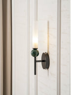 The Clérachic wall light lit on a panelled wall, curtain falling to the left and its glow washing the panel behind it.