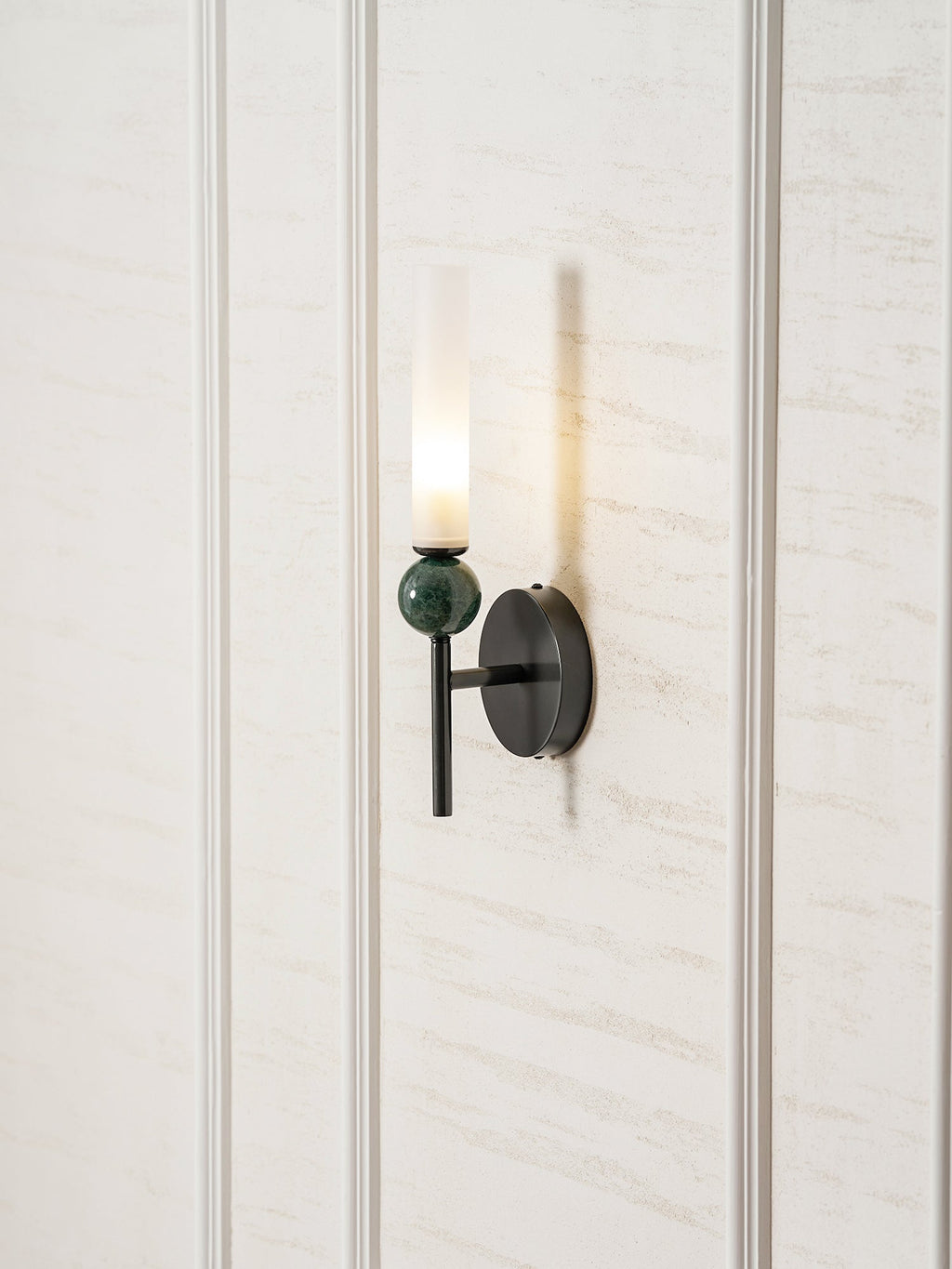 Centred on a pale panelled wall, the lit Clérachic wall light casts a narrow shadow beside its frosted cylinder.
