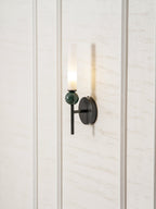 Centred on a pale panelled wall, the lit Clérachic wall light casts a narrow shadow beside its frosted cylinder.