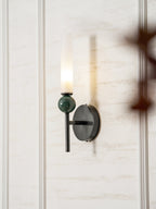 A blurred branch crosses the foreground while the Clérachic wall light glows against the panelling behind it.