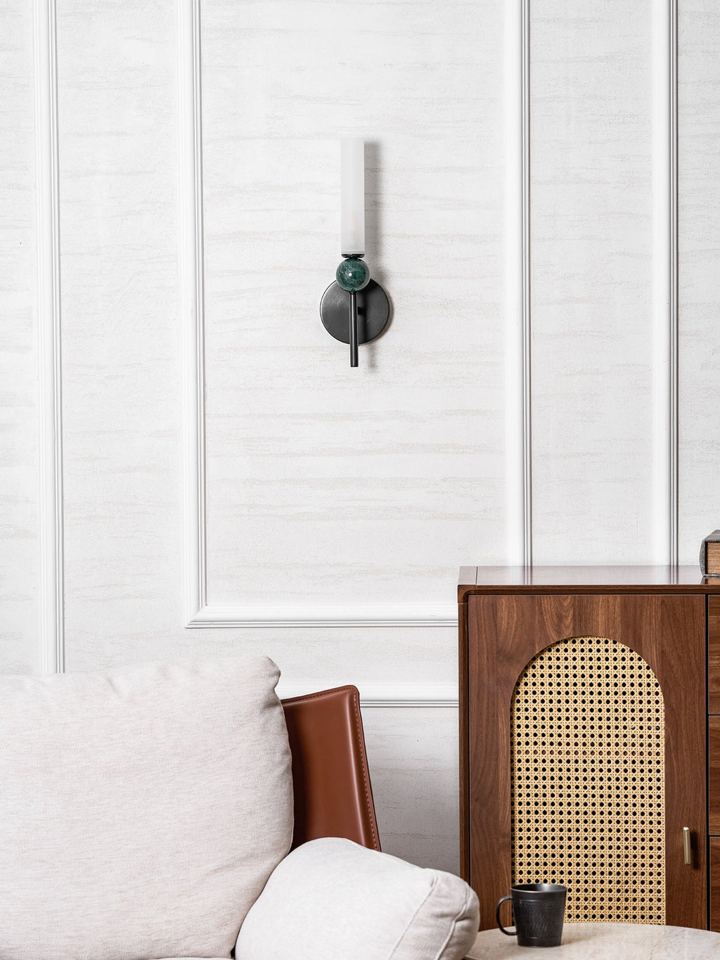 Seen across a room, the Clérachic wall light sits high on the panelling above a leather chair and a cane-fronted cabinet.