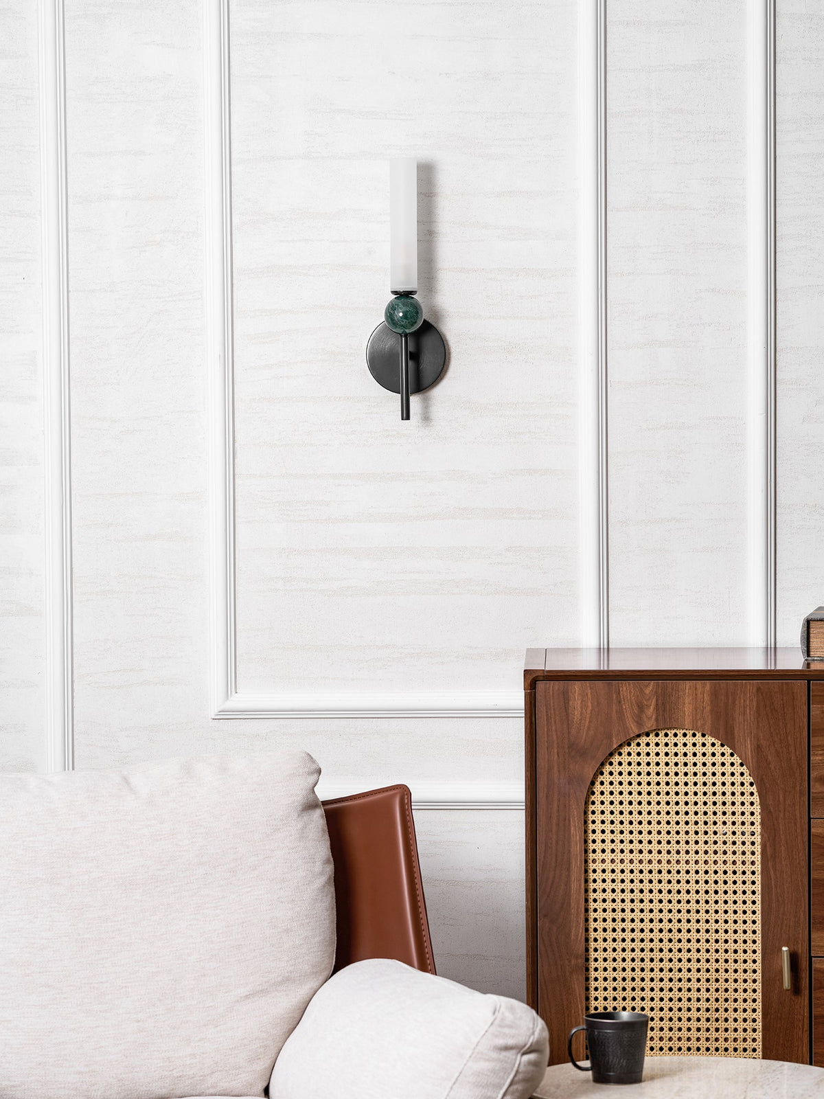 Seen across a room, the Clérachic wall light sits high on the panelling above a leather chair and a cane-fronted cabinet.