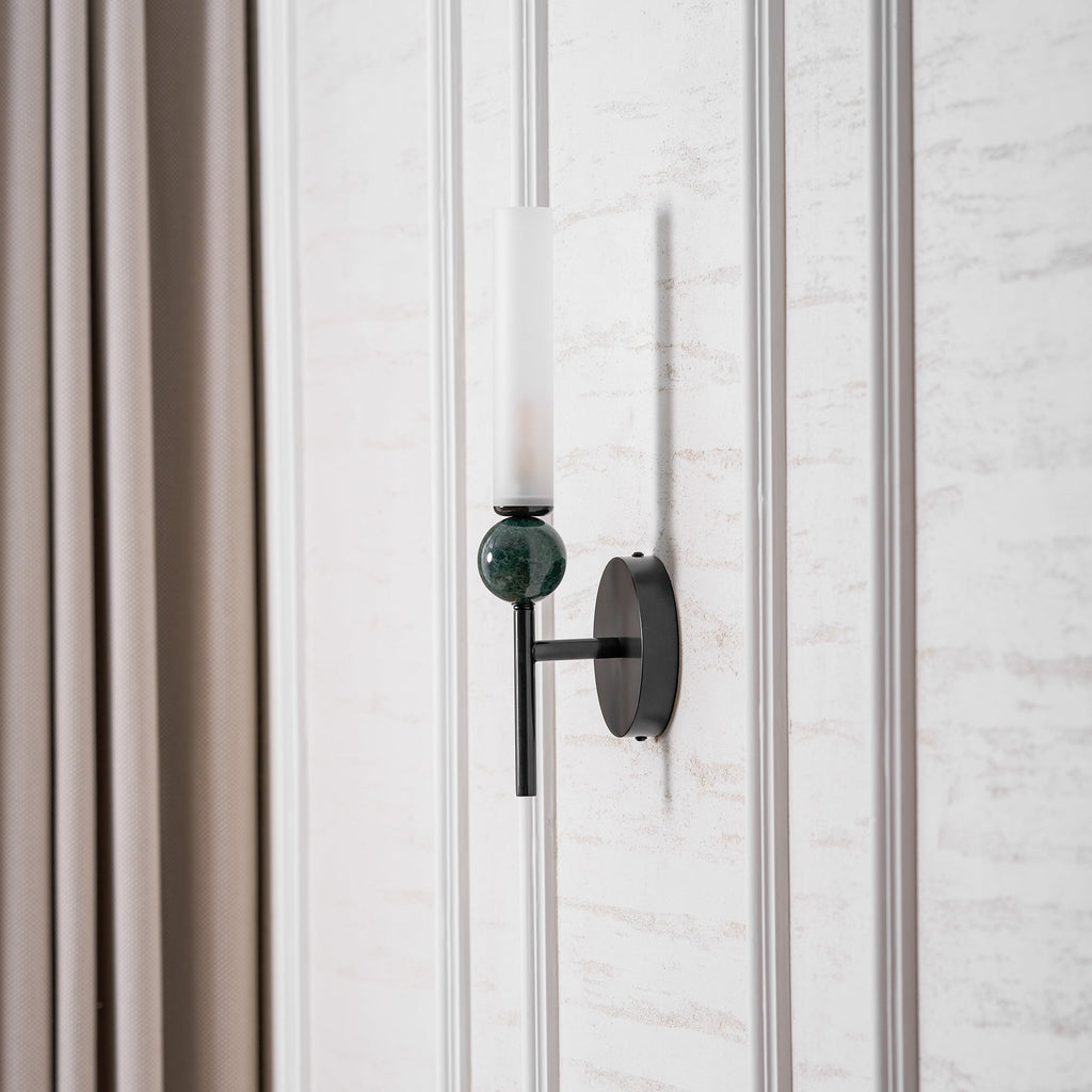 Beside a full-length curtain, the Clérachic wall light is lit, its green marble sphere catching the warm glow above it.