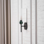 Beside a full-length curtain, the Clérachic wall light is lit, its green marble sphere catching the warm glow above it.