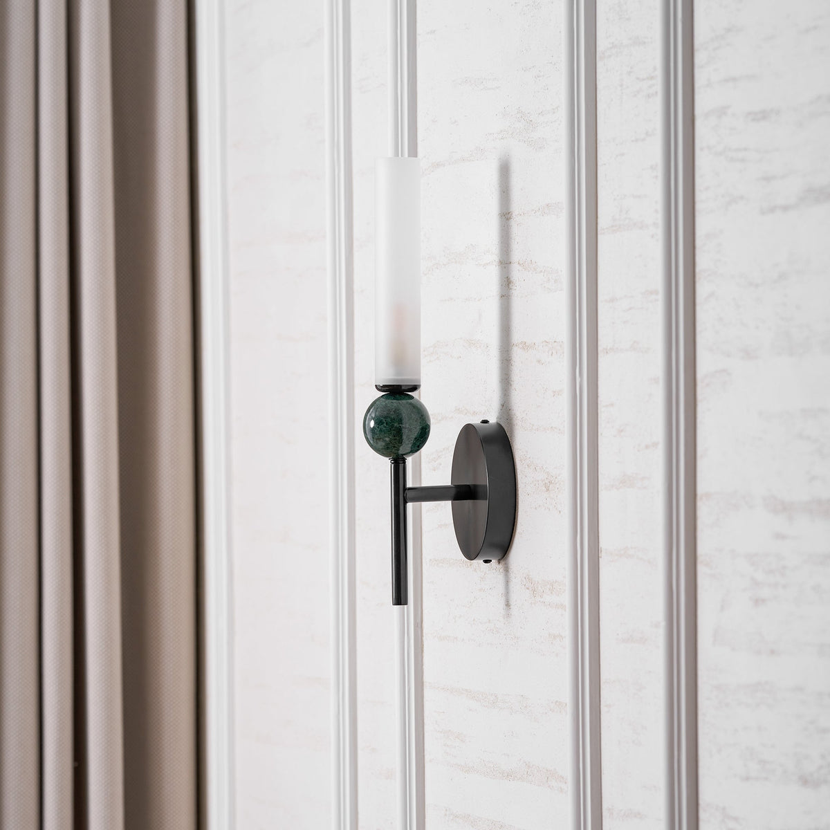 Beside a full-length curtain, the Clérachic wall light is lit, its green marble sphere catching the warm glow above it.