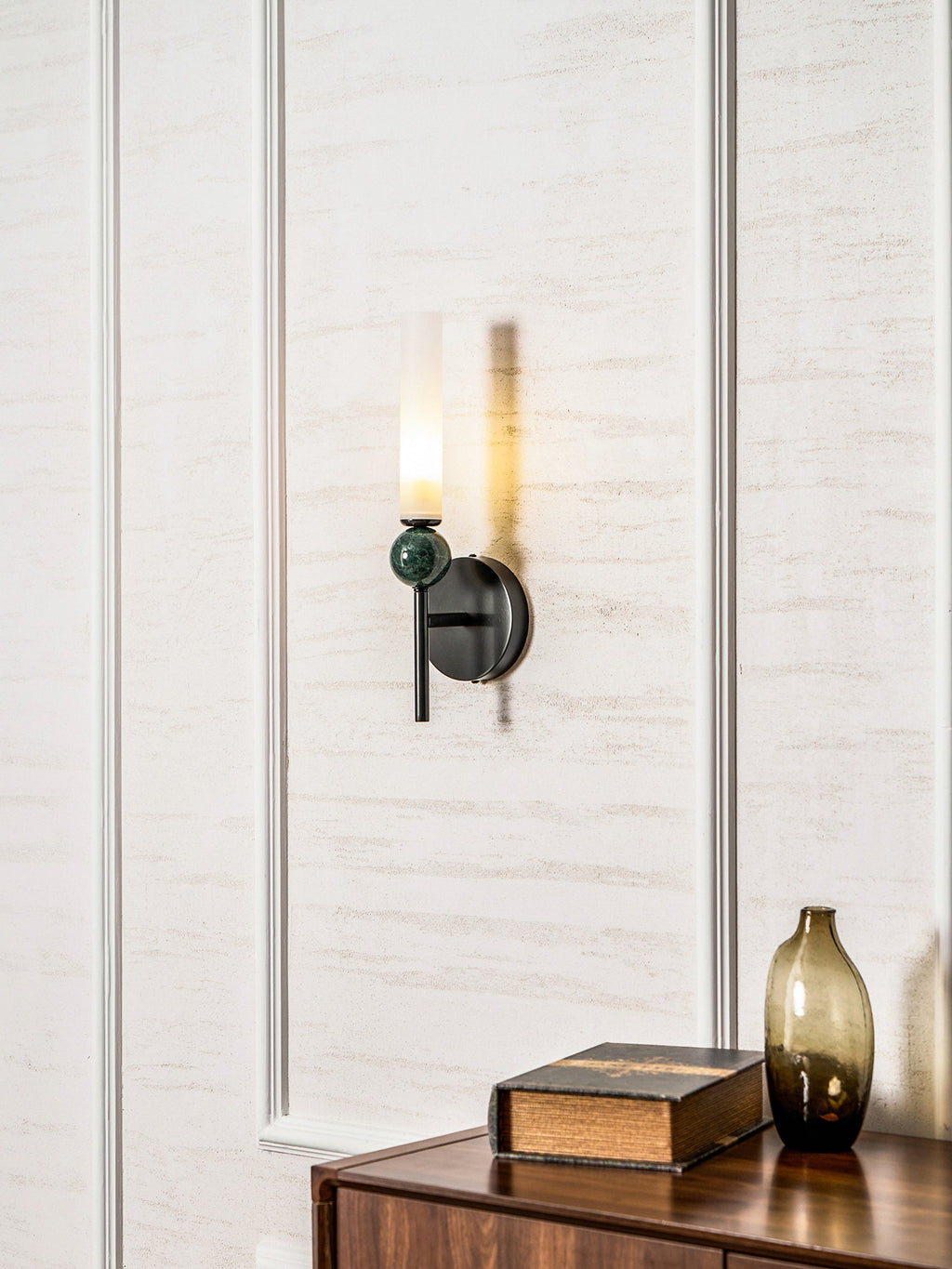 Above a walnut cabinet holding a book and a green glass vase, the Clérachic wall light lights the panel it is fixed to.
