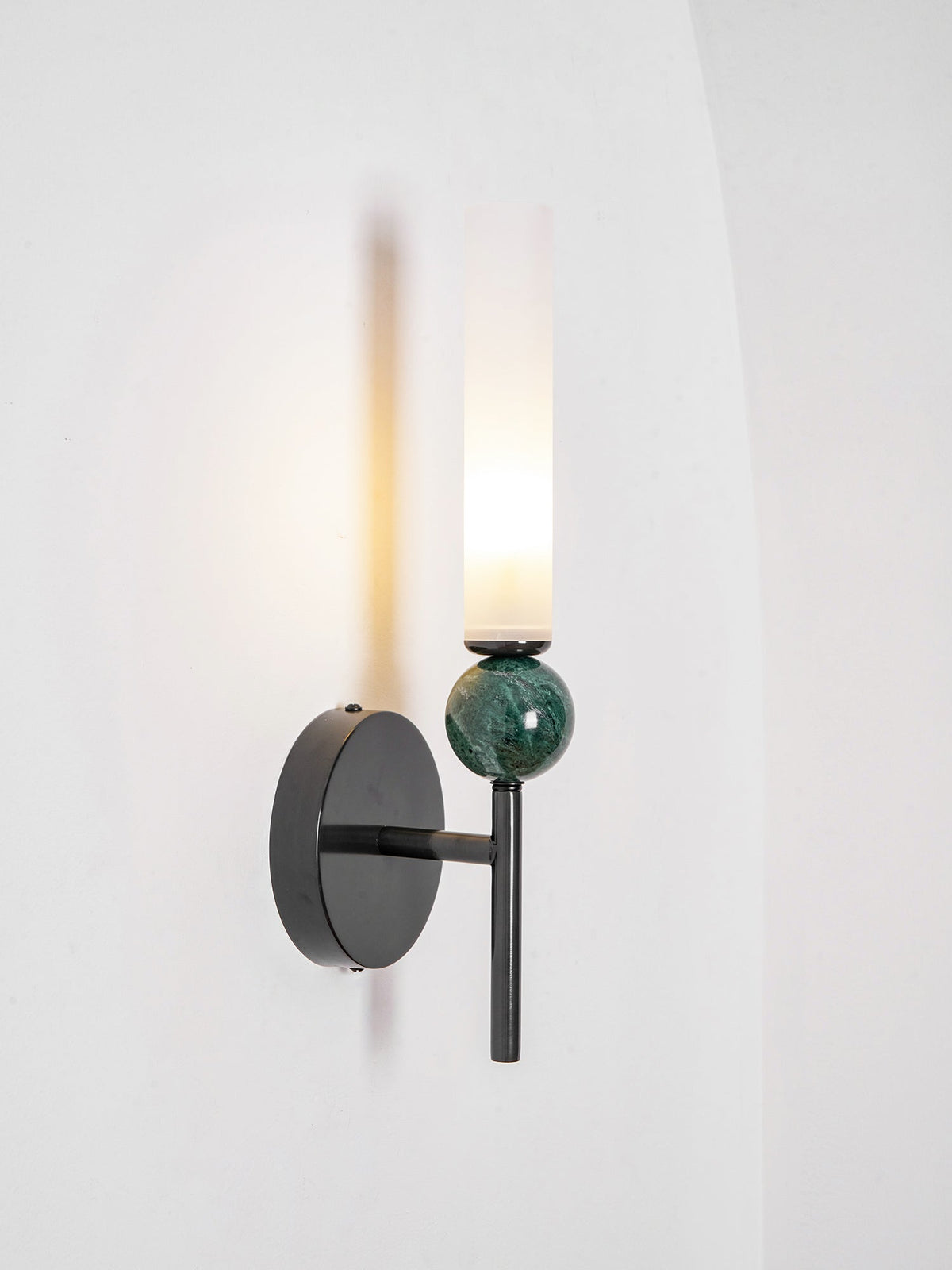 Three-quarter view of the lit Clérachic wall light, the black disc set back from the green marble and glass in front.