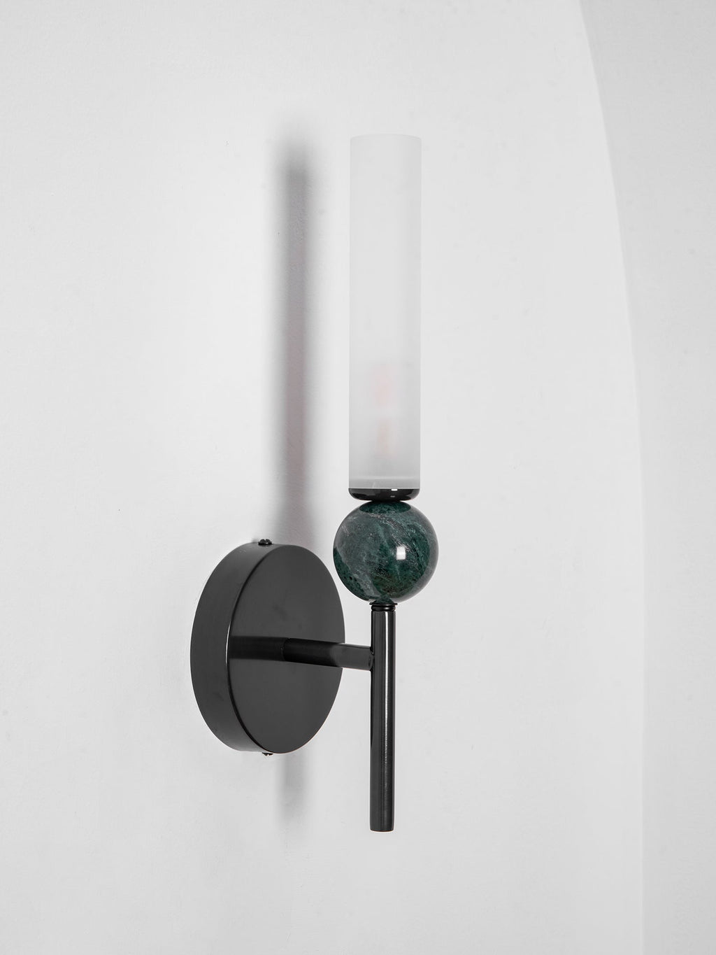 Unlit and angled, the Clérachic wall light shows its clear glass cylinder, green marble sphere and black disc backplate.
