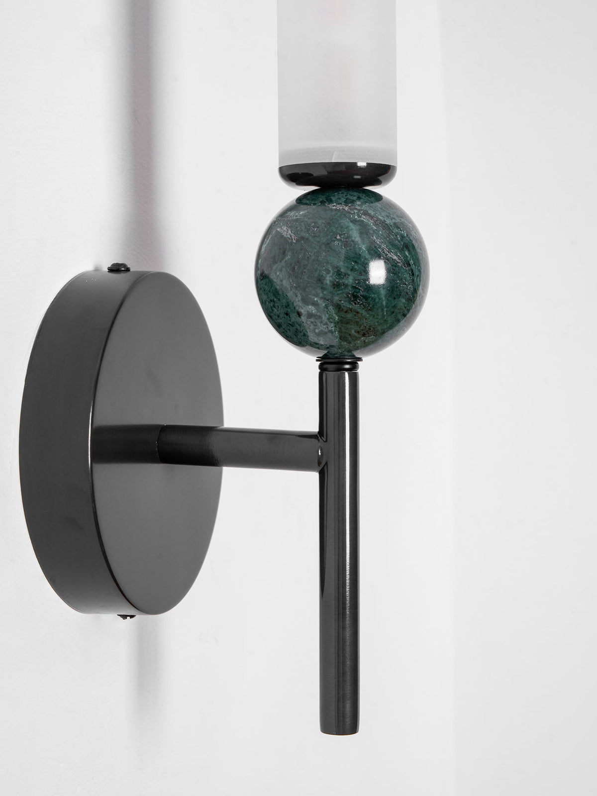 Macro detail of a Clérachic wall light's black rod meeting a green marble orb with white veining beneath the frosted shade.
