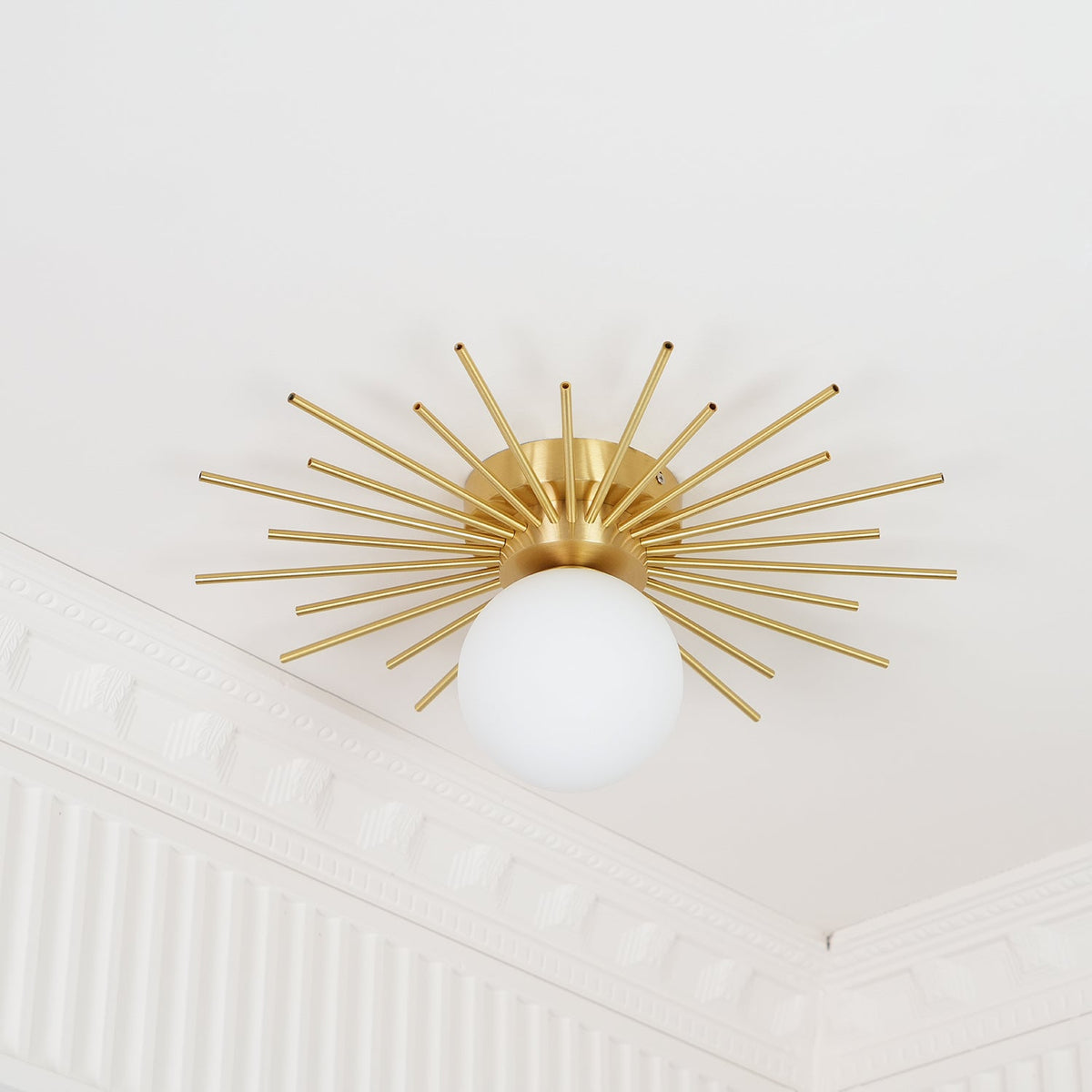 Positioned in a corner with crown moulding, this Clérachic ceiling light has its globe beneath the brass rays.