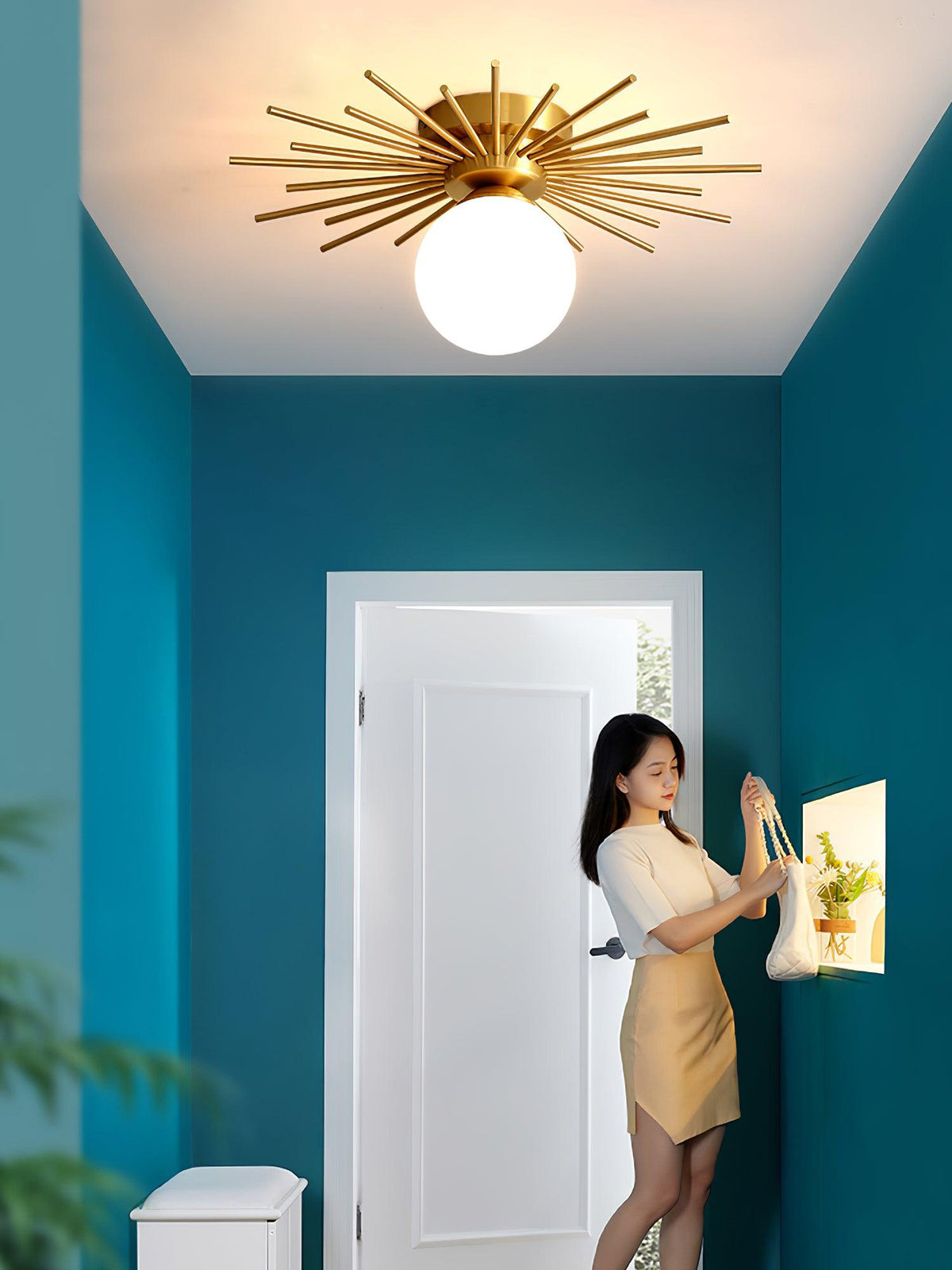 In a teal hallway, this Clérachic ceiling light shines as a woman adjusts a framed picture by the door.