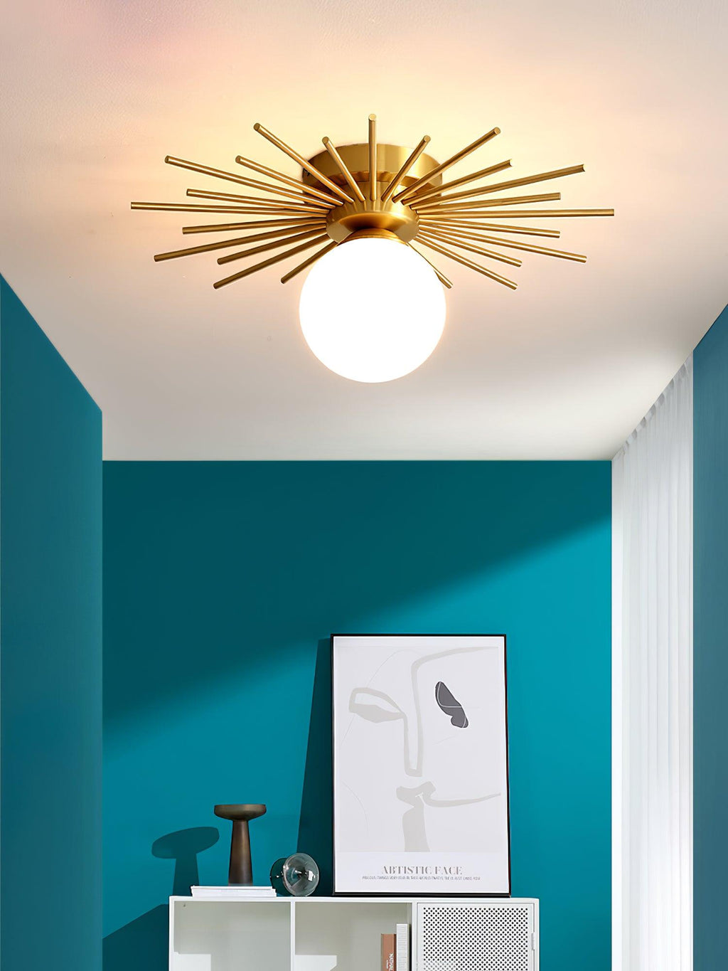 A framed print and bird sculpture sit on a white cabinet beneath this Clérachic ceiling light, against a teal wall.