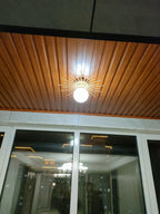 Mounted on a wood-panelled ceiling, this Clérachic ceiling light glows warm against tall night-lit windows.