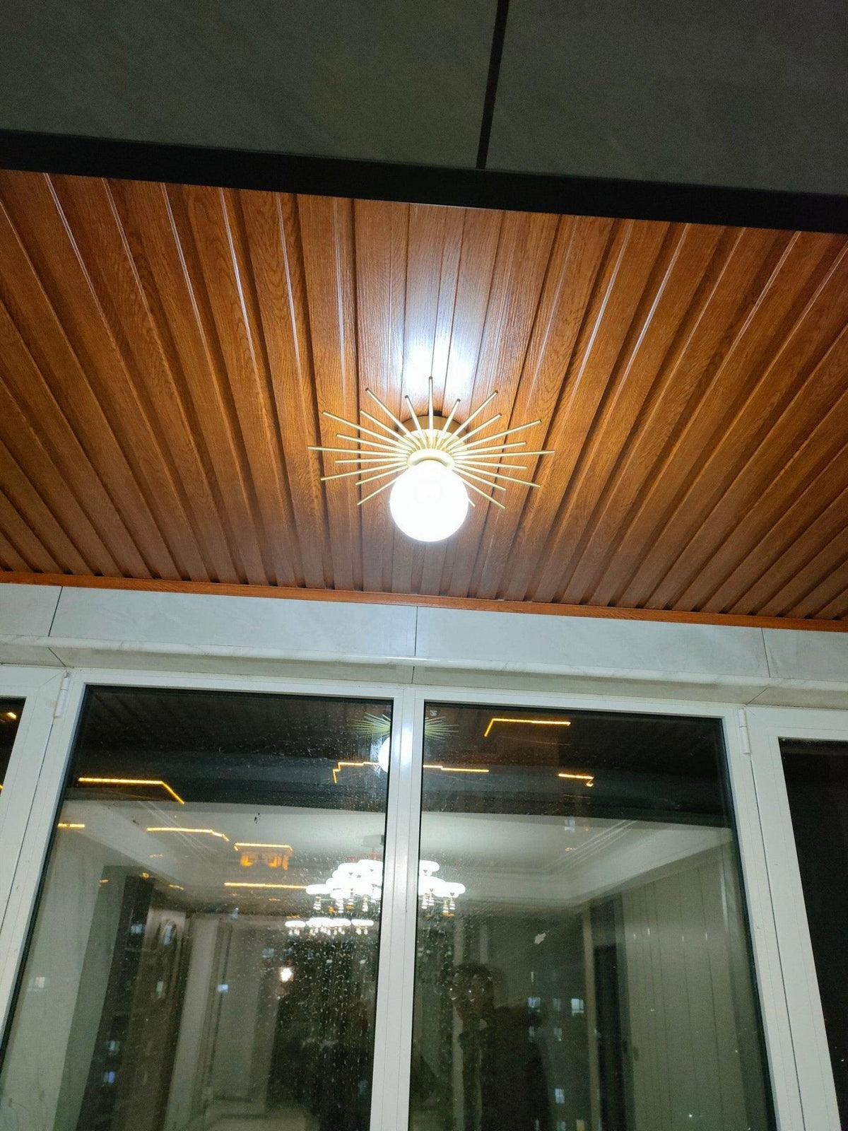 Mounted on a wood-panelled ceiling, this Clérachic ceiling light glows warm against tall night-lit windows.