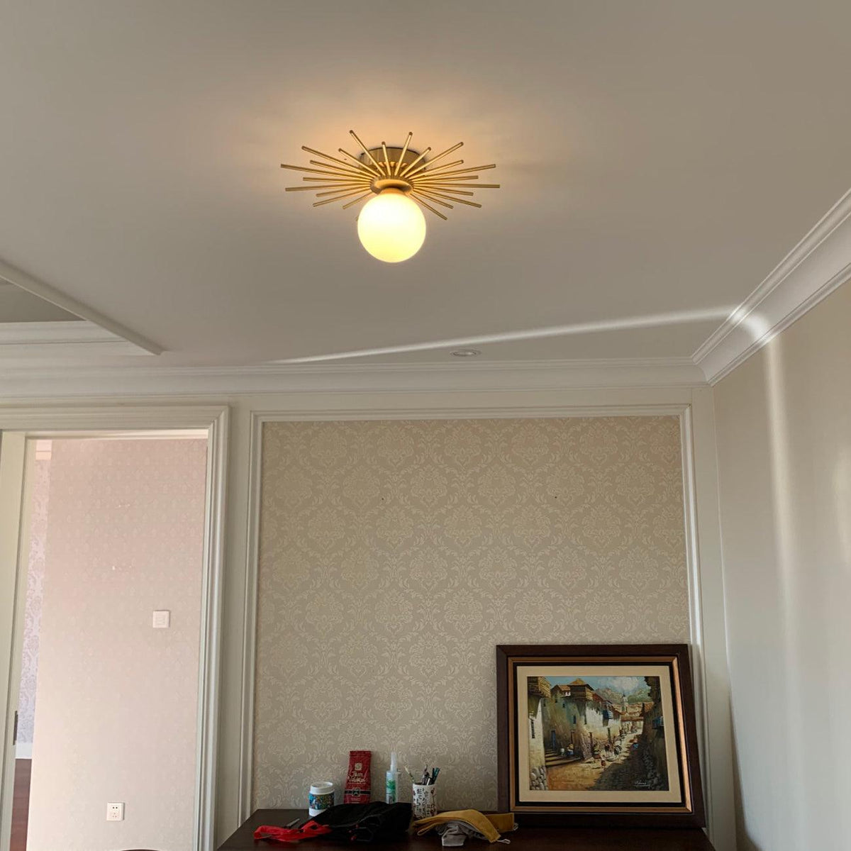 This Clérachic ceiling light lights a small room papered in a pale damask print, a framed painting below.