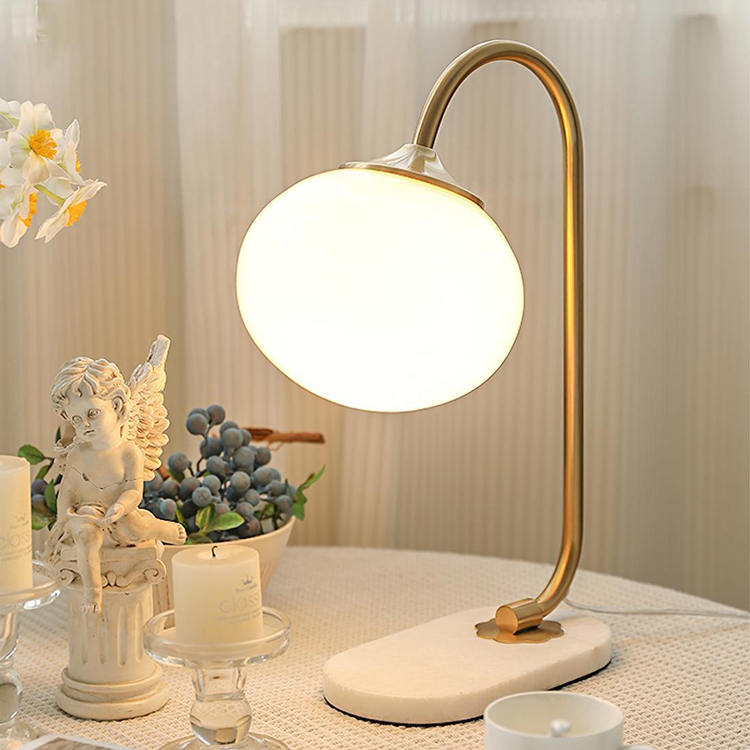 The Clérachic table lamp's white shade glows beside a cherub figurine, dark berries and a lit candle on a dressed side table.