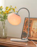 A peach glass shade tops the Clérachic table lamp's chrome arm, set among yellow daisies in a glass vase on a dark wood console.