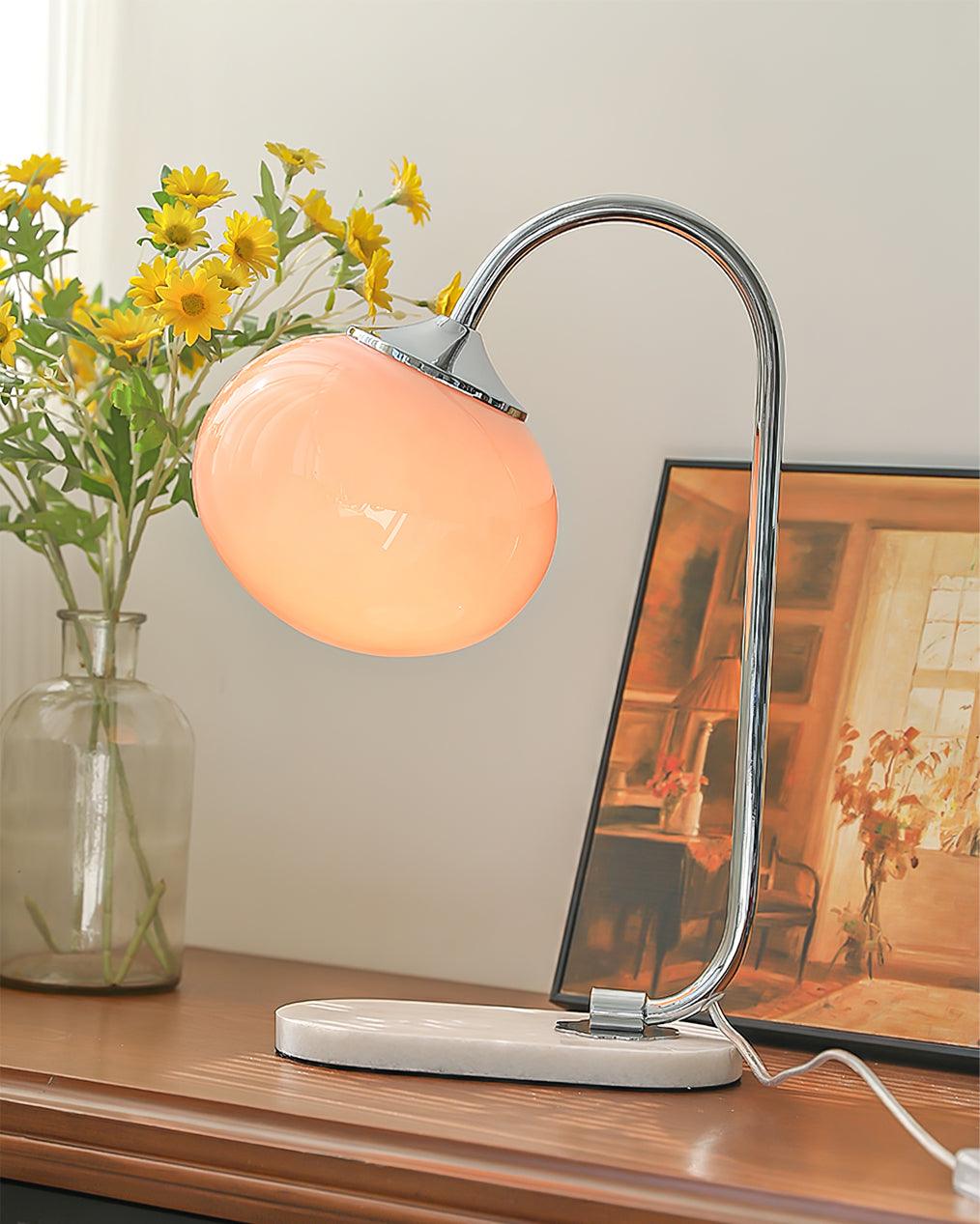 A peach glass shade tops the Clérachic table lamp's chrome arm, set among yellow daisies in a glass vase on a dark wood console.