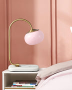 The Clérachic table lamp's pink shade sits on a marble-topped nightstand against a dusty pink wall, folded bedding visible behind it.