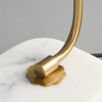 Close-up of the Clérachic table lamp's gold arm meeting its marble base, showing the flower-shaped mounting plate and hardware.