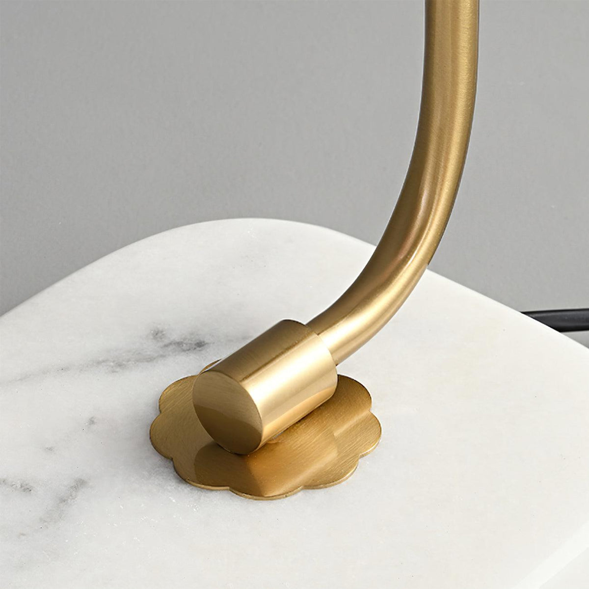 Close-up of the Clérachic table lamp's gold arm meeting its marble base, showing the flower-shaped mounting plate and hardware.
