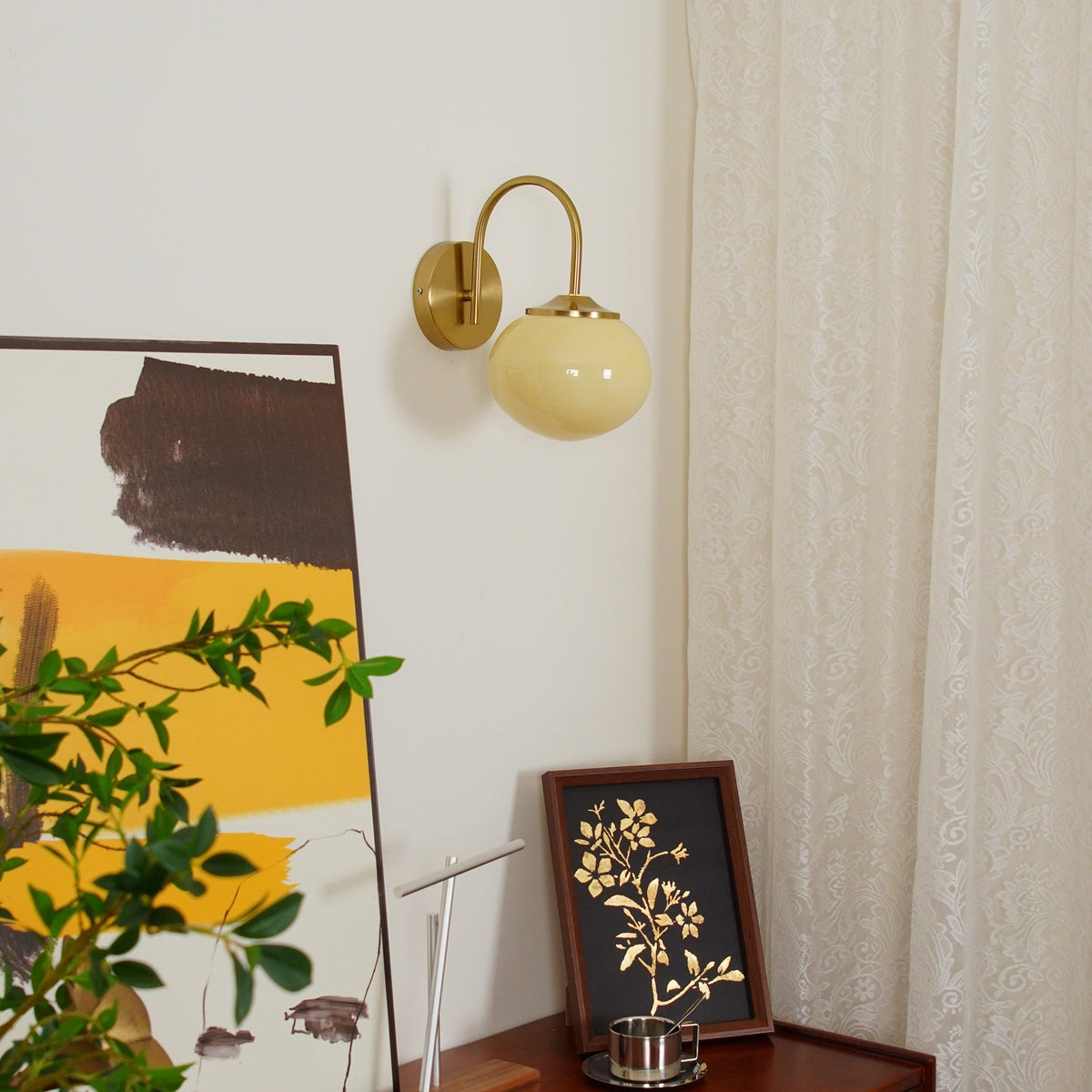 Trailing greenery and framed art flank this Clérachic wall light in copper and white glass, unlit.