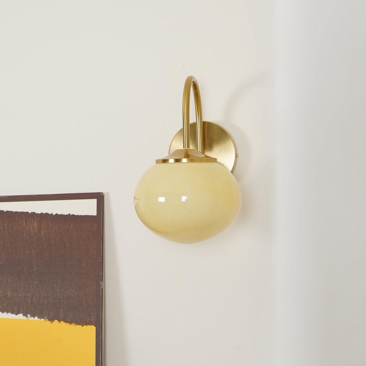 Abstract art in mustard and brown tones sits beside this Clérachic wall light in copper and beige glass, unlit.