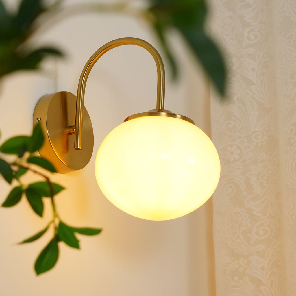 Trailing leaves brush this Clérachic wall light in copper and white glass, lit, against sheer curtains.