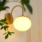 Trailing leaves brush this Clérachic wall light in copper and white glass, lit, against sheer curtains.