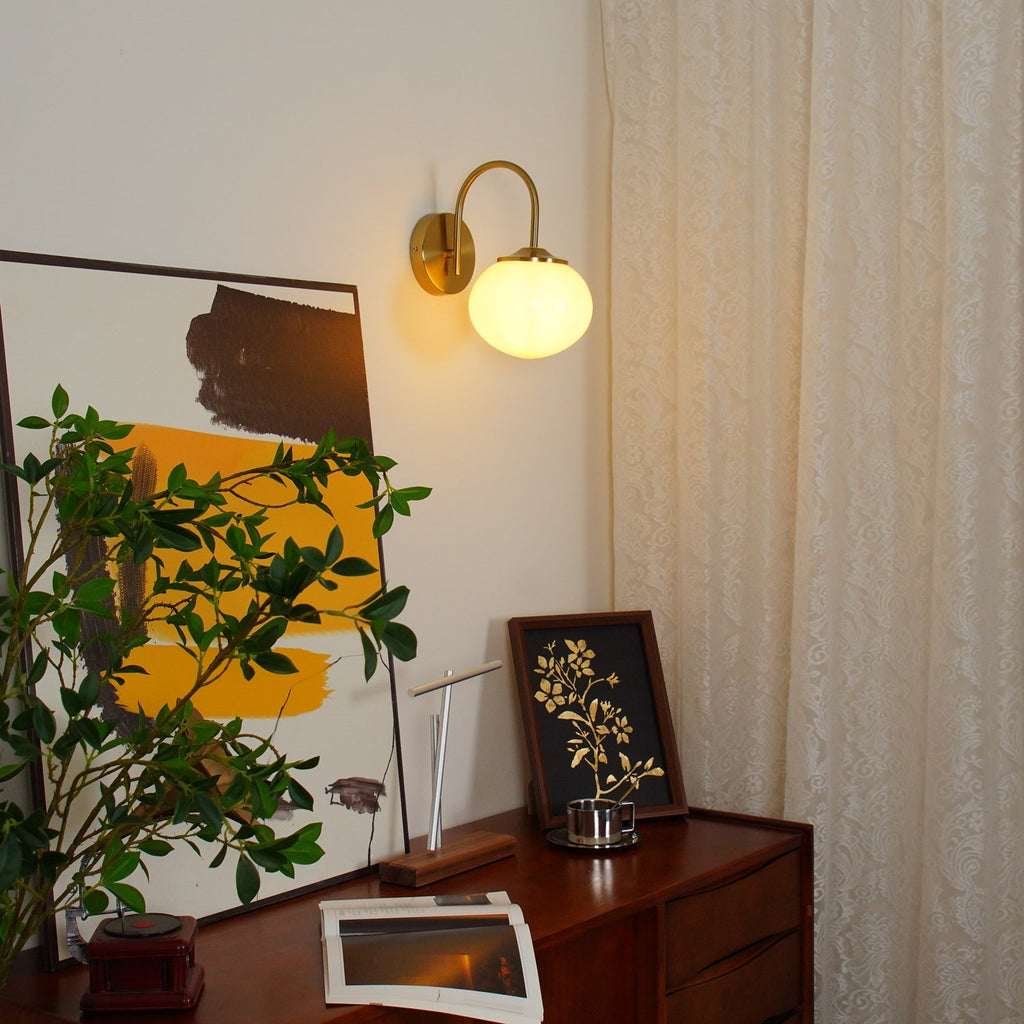 Above a wooden console with a potted plant, this Clérachic wall light in copper and white glass glows warm.
