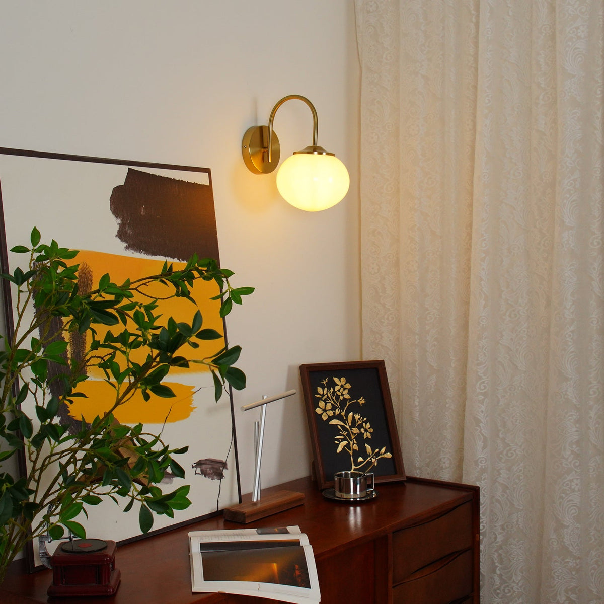 Above a wooden console with a potted plant, this Clérachic wall light in copper and white glass glows warm.