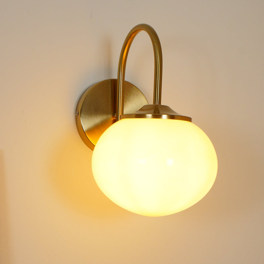 This Clérachic wall light in copper and white glass glows warm on a plain cream wall.