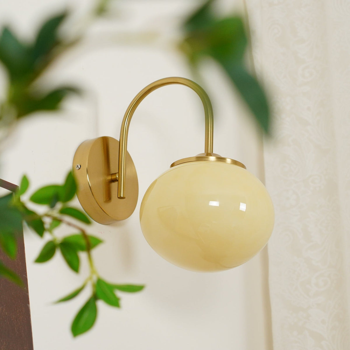 Trailing green leaves frame this Clérachic wall light in copper and beige glass, unlit, shown at an angle.