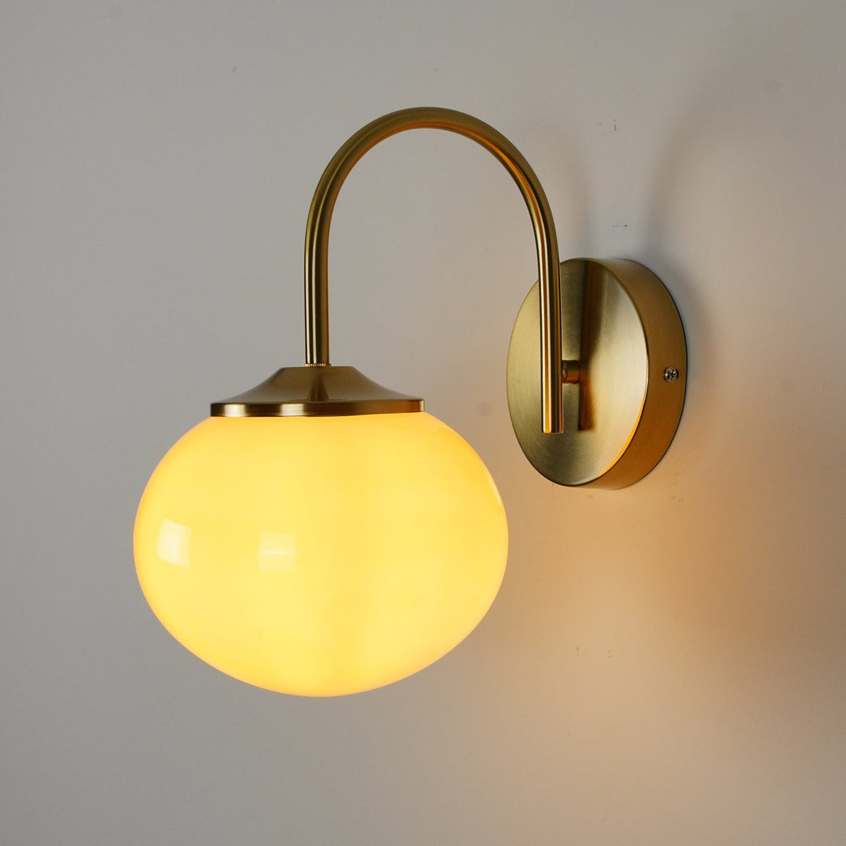 Warm light glows from this Clérachic wall light in copper and white glass, mounted on a grey wall.