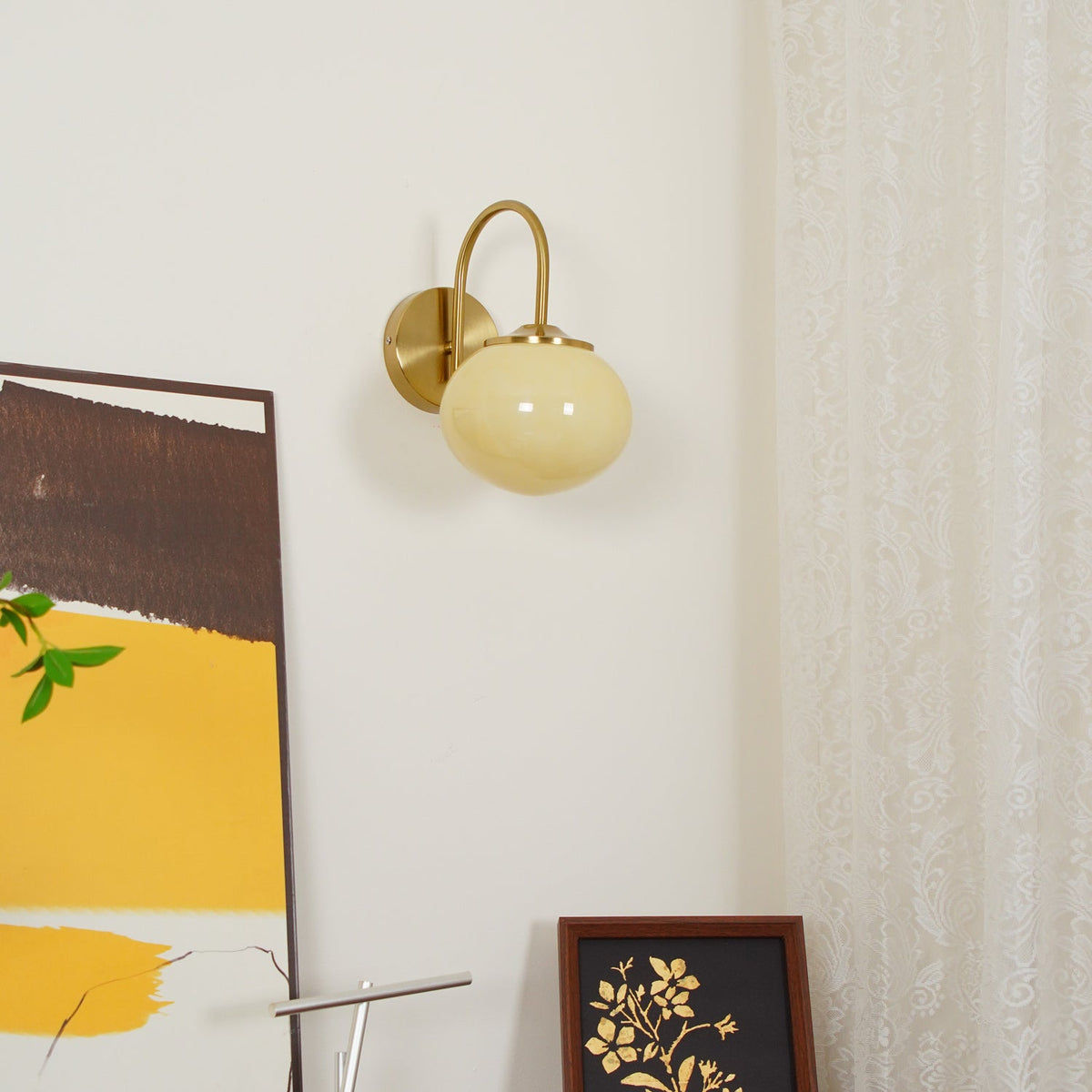 Mustard and brown abstract art hangs beside this Clérachic wall light in copper and beige glass, unlit.