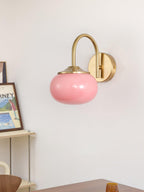 Framed art sits on a shelf beneath this Clérachic wall light in copper and pink glass, on a plain white wall.