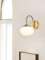Near a window, this Clérachic wall light in copper and white glass hangs beside a framed picture.
