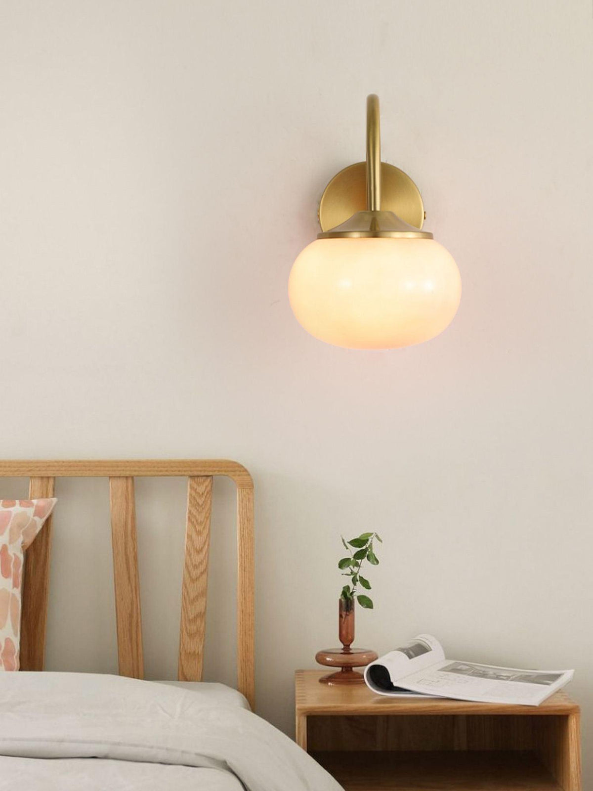 Beside a wooden bed frame, this Clérachic wall light in copper and beige glass glows warm above a nightstand with a book.