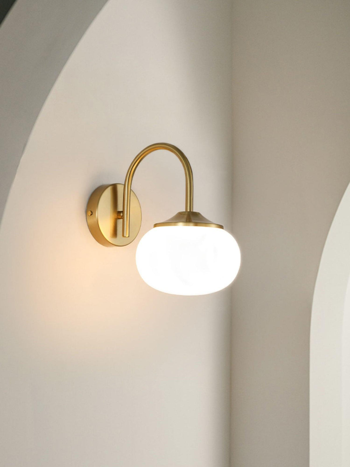 Mounted in a curved alcove, this Clérachic wall light in copper and white glass sits unlit against a soft grey wall.