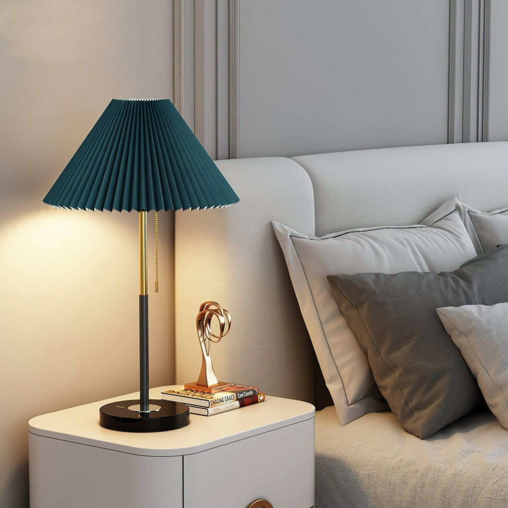 Same Clérachic lamp shown in a dark teal pleated shade, lit on the bedside cabinet beside the same books and sculpture.
