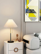Clérachic lamp lit beside framed geometric art, its cream pleated shade glowing on the bedside cabinet.
